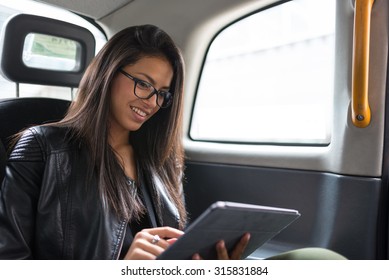 Smiling Portrait Of Young Mixed Race Businesswoman Inside A Taxi In Canary Wharf Area In London While Using A Tablet.