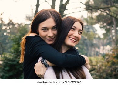 Smiling portrait of young sisters hugging outdoors in a park.