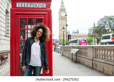Smiling portrait of young woman close to red telephone box in London. Big Ben in the background.