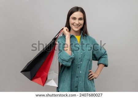 Smiling positive attractive woman standing with smile, holding shopping bags in her hands, being happy, wearing casual style jacket. Indoor studio shot isolated on gray background.