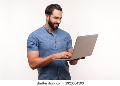 Smiling Positive Man Holding Laptop In Hand And Typing, Blogger Making Posts In Social Networks, Chatting With Followers. Indoor Studio Shot Isolated On White Background