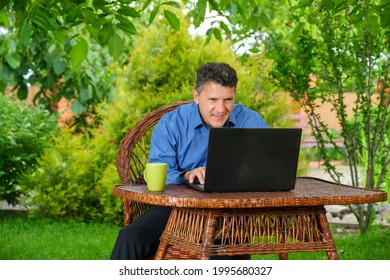 Smiling positive middle-aged businessman reading good finance news using laptop sitting in his backyard garden. Remote working concept  - Shutterstock ID 1995680327