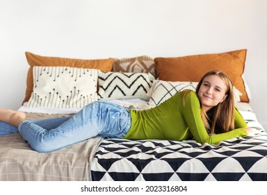 Lächelnd positives Mädchen in ungezwungenen Kleidung auf dem Bett liegen in ihrem gemütlichen Zimmer zu Hause, nach der Universität ruhen, schöne junge Frau entspannen im Schlafzimmer, verbringen Freizeit allein