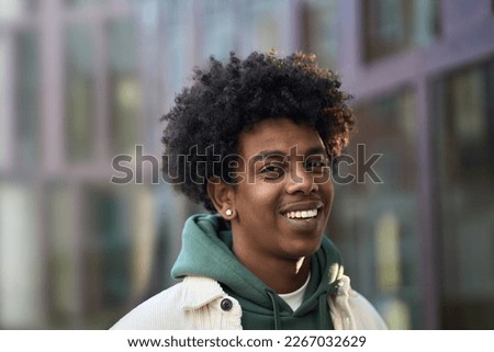 Smiling positive young African American guy model standing at big city street. Stylish ethnic hipster gen z teenager boy feeling happy looking at camera outdoors, close up portrait.