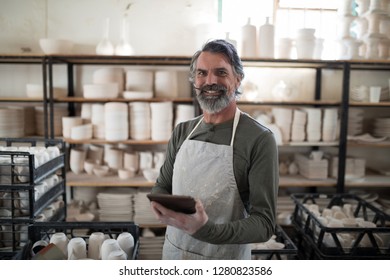 Smiling potter using tablet surrounded by work in the pottery workshop