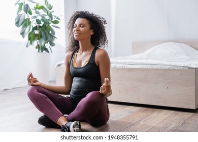 Smiling pregnant african american woman sitting in yoga pose in bedroom