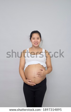 Smiling pregnant Asian woman touching her belly on grey background