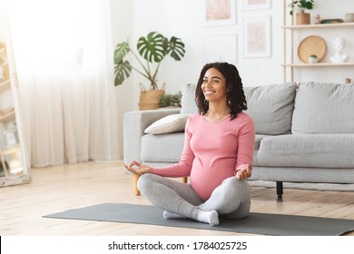 Smiling pregnant black woman sitting in lotus pose at home, having healthy lifestyle during pregnancy, free space