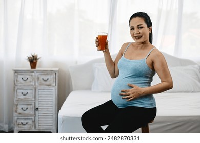 Smiling pregnant woman in blue tank top holding glass of orange juice, health, happiness, and well-being during pregnancy with copy space - Powered by Shutterstock