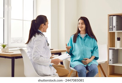 Smiling pregnant woman sitting at the desk in doctor's office visiting obstetrician in maternity clinic. Gynecologist holding report file and giving consultation during medical exam. - Powered by Shutterstock