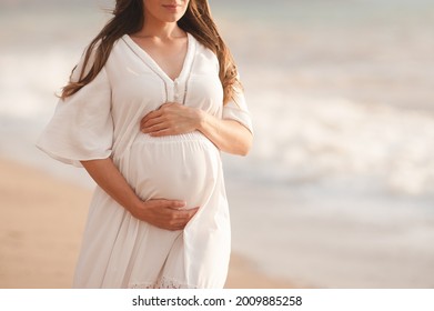 Smiling pregnant woman wear white dress hol tummy walk at beach over sea nature background outdoors. Summer vacation season. Motherhood. Maternity. Happiness.  - Powered by Shutterstock