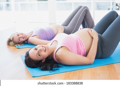 Smiling pregnant women in yoga class lying on mats in a fitness studio