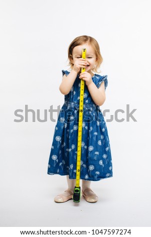 A smiling preschool girl holding a measuring tape in front of her, grow so fast
