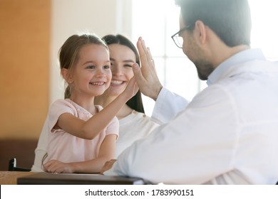 Smiling preschool girl sitting on mum laps, giving high five to male pediatrician at meeting in clinic, friendly therapist gp greeting welcoming little patient at consultation, celebrate good result - Powered by Shutterstock