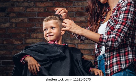 Smiling preschooler boy getting a haircut. Children hairdresser with scissors and comb is cutting little boy in the room with loft interior. - Powered by Shutterstock