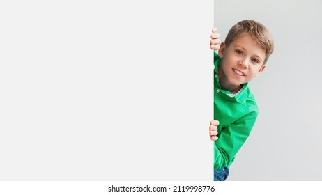 Smiling Preteen Boy Posing With Blank White Poster Board Peeking Looking At Camera On Gray Studio Background. Schoolboy Advertising Your Text. Mockup, Panorama With Copy Space - Shutterstock ID 2119998776