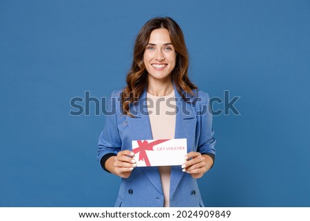Smiling pretty beautiful attractive young brunette woman 20s in basic casual jacket standing holding in hand gift certificate looking camera isolated on bright blue colour background studio portrait