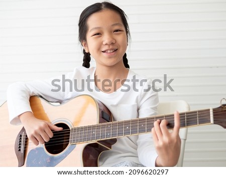 Smiling pretty girl child and acoustic guitar isolated on white background. Kid guitarist put fingers on the fingerboard of string instrument playing fingerpicking melody sound. A talented little girl