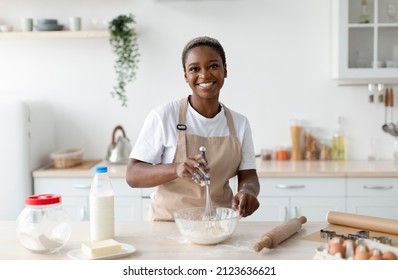 Smiling Pretty Millennial African American Woman Chef In Apron Making Dough In Light Minimalist Kitchen Interior, Copy Space. Baking, Food Blog, New Recipe For Cooking At Home During Covid-19 Lockdown