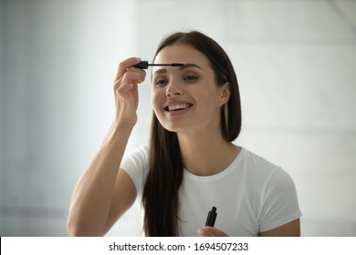 Smiling Pretty Millennial Girl Look In Mirror Paint Eyelashes With Black Thickening Volume Mascara, Happy Beautiful Young Woman Get Ready In Bathroom Do Make Up Daily Morning Routine In Bath At Home