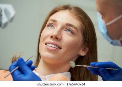 A smiling pretty woman being examined by a dentist in a medical face mask with a dental mirror and a dental explorer in a dental chair. A doctor treating a patient's teeth in a dentist's office.