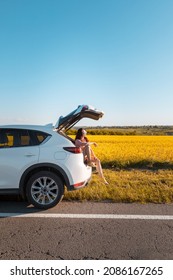 smiling pretty woman sitting in suv car trunk on sunset looking at farm field road trip concept - Shutterstock ID 2086167265