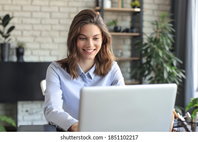 Smiling pretty woman sitting at table, looking at laptop screen. Happy entrepreneur reading message email with good news, chatting with clients online. - Powered by Shutterstock