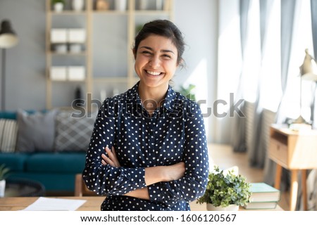 Smiling pretty young adult indian woman looking at camera posing at modern home arms crossed, cheerful happy ethnic girl student self employed lady laughing enjoying distance job education, portrait ストックフォト © 