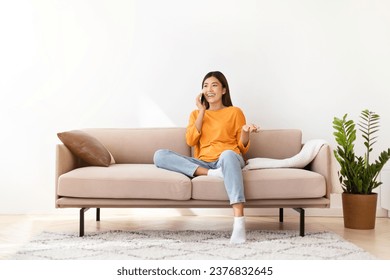 Smiling pretty young asian woman talking on phone at home. Happy chinese lady have conversation, using mobile phone, laughing during funny call with boyfriend, looking at copy space. Communication - Powered by Shutterstock