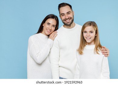 Smiling pretty young happy parents mom dad with child kid daughter teen girl in basic white sweaters hugging isolated on blue color background studio portrait. Family day parenthood childhood concept