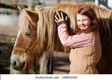 Smiling pretty young teenage girl standing grooming the mane of her horse with a brush in the sunshine in an outdoor paddock - Powered by Shutterstock