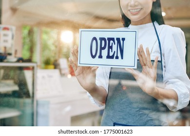 Smiling Pretty Young Waitress Sticking Open Sign On Glass Door Of Coffeeshop