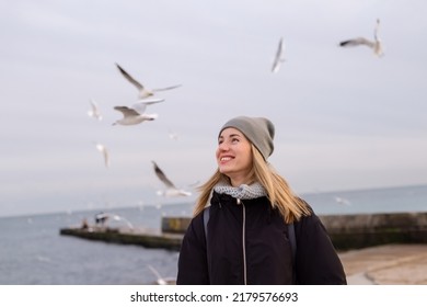 smiling pretty young woman on winter seashore looking at seagulls  - Powered by Shutterstock