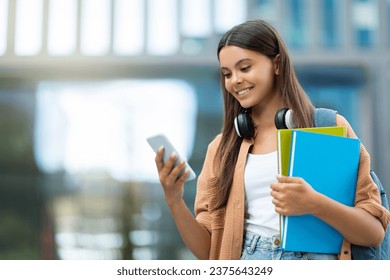 Smiling pretty young woman student using app on smartphone, navigates through an educational app on her smartphone, blending learning and technology at a bustling university campus, copy space - Powered by Shutterstock