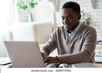 Smiling Professional Black Business Man Using Laptop Computer Working From Home Office. Happy African Male Customer Makes Ecommerce Delivery Order From Supermarket Typing On Pc Sits At Kitchen Table.