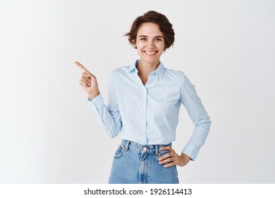 Smiling Professional Ceo Woman In Blue Collar Shirt, Pointing Finger Left At Logo And Looking Confident At Camera, Standing On White Background.