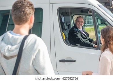 Smiling Professional Driver In Van Looking At Passengers At Airport