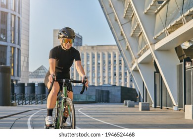 Smiling Professional Female Cyclist In Black Cycling Garment And Protective Gear Looking Satisfied With Her Exersicing Outdoors On A Sunny Day