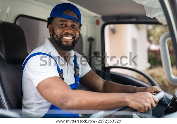 Smiling professional\
man mover worker in blue uniform driving truck to delivery and\
moving house service