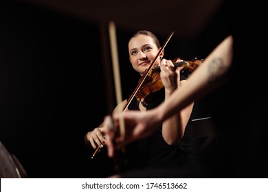 Smiling Professional Musicians Playing Classical Music On Violins On Dark Stage