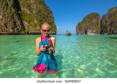 Smiling Professional Photographer With Colorful Blue And Pink Sarong, Checks His Camera. Maya Bay, Famous Lagoon Of The Beach Movie With Leonardo DiCaprio, Phi Phi Leh, Andaman Sea In Thailand.