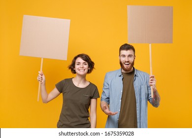 Smiling protesting young two people guy girl hold protest signs broadsheet blank placard on stick isolated on yellow background studio portrait. Protests strikes pickets concept. Youth against city