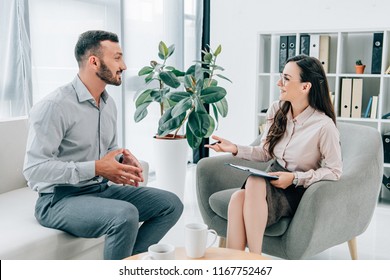 Smiling Psychiatrist With Clipboard Talking With Happy Patient In Office