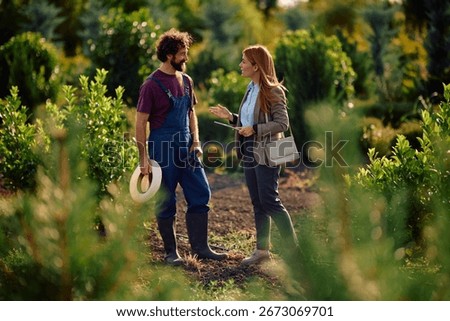 Smiling quality control inspector talking to a worker while examining tree saplings in the field. 