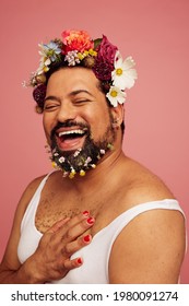 Smiling queer wearing makeup and tank top. Cheerful drag queen wearing flowers in his head and beard.