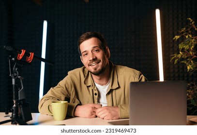 Smiling radio host  into studio microphone at radio station with neon lights  looking at camera