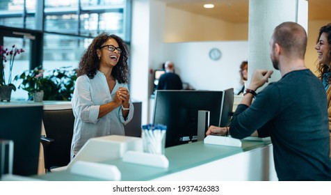 Smiling Receptionist Assisting People Standing At Municipal Office Reception Desk. Administrator Smiling While Discussing With People At Municipality Office.