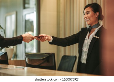Smiling receptionist behind the hotel counter attending female guest. Concierge giving the documents to hotel guest.