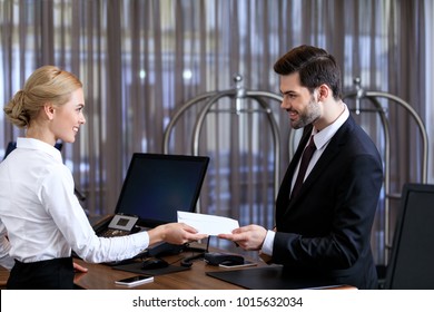 smiling receptionist giving envelope to businessman in hotel