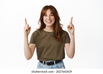 Smiling Redhead Woman Pointing Fingers Up Happy, Standing In Green Tshirt Against White Background